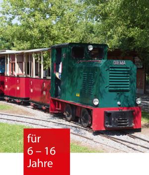 eine grüne alte Feldbahn zieht zwei offene kleine Waggons über Schienen