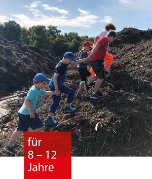 Vier Kinder laufen mit einem Mitarbeiter einen Berg aus Erde/Kompost hinauf