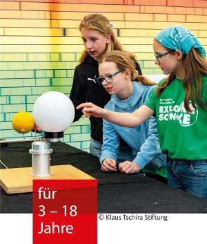 Drei Mädchen schauen interessiert ein Experiment mit einer weißen und gelben Kugel an