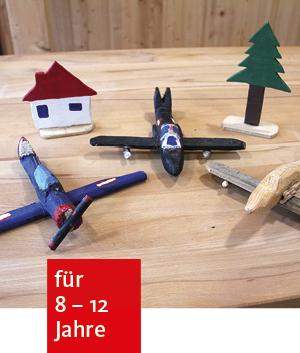 auf einen Holztische liegt selbstgebasteltes Spielzeug aus Holz: 3 Flieger, ein Häuschen, ein Tannenbaum