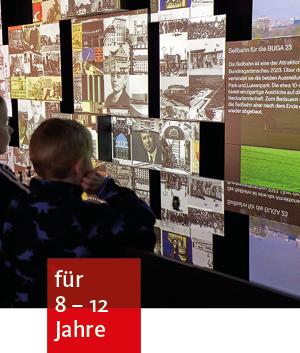 ein Kind steht in einem dunklen Raum vor einer großen Bildschirmleinwand mit verschiedenen digitalen Abbildungen