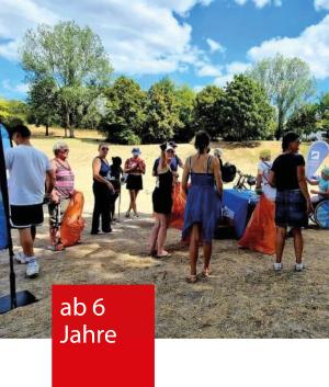 Eine Gruppe von Menschen steht auf einer Wiese. Sie haben orangene Müllbeutel und Zangen zum Abfall sammeln in der Hand.