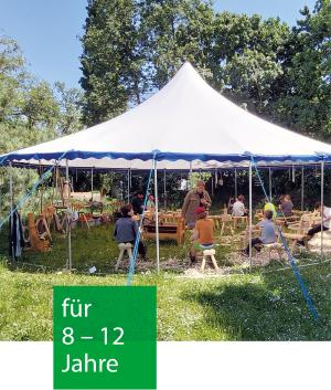 Unter einem Zeltdach in der grünen Natur sitzen Kinder an Ziehholzbänken und bearbeiten Holz oder schnitzen.