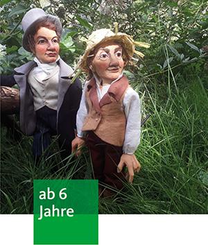 zwei als Herren gekleidete Holzpuppen stehen im hohen Gras