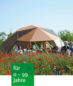 in einem Mohnfeld steht ein Holziglu vor dem viele Menschen stehen