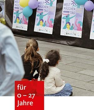 zwei Mädchen sitzen auf dem Alten Messplatz und schauen sich Plakate an zum Weltmädchentag